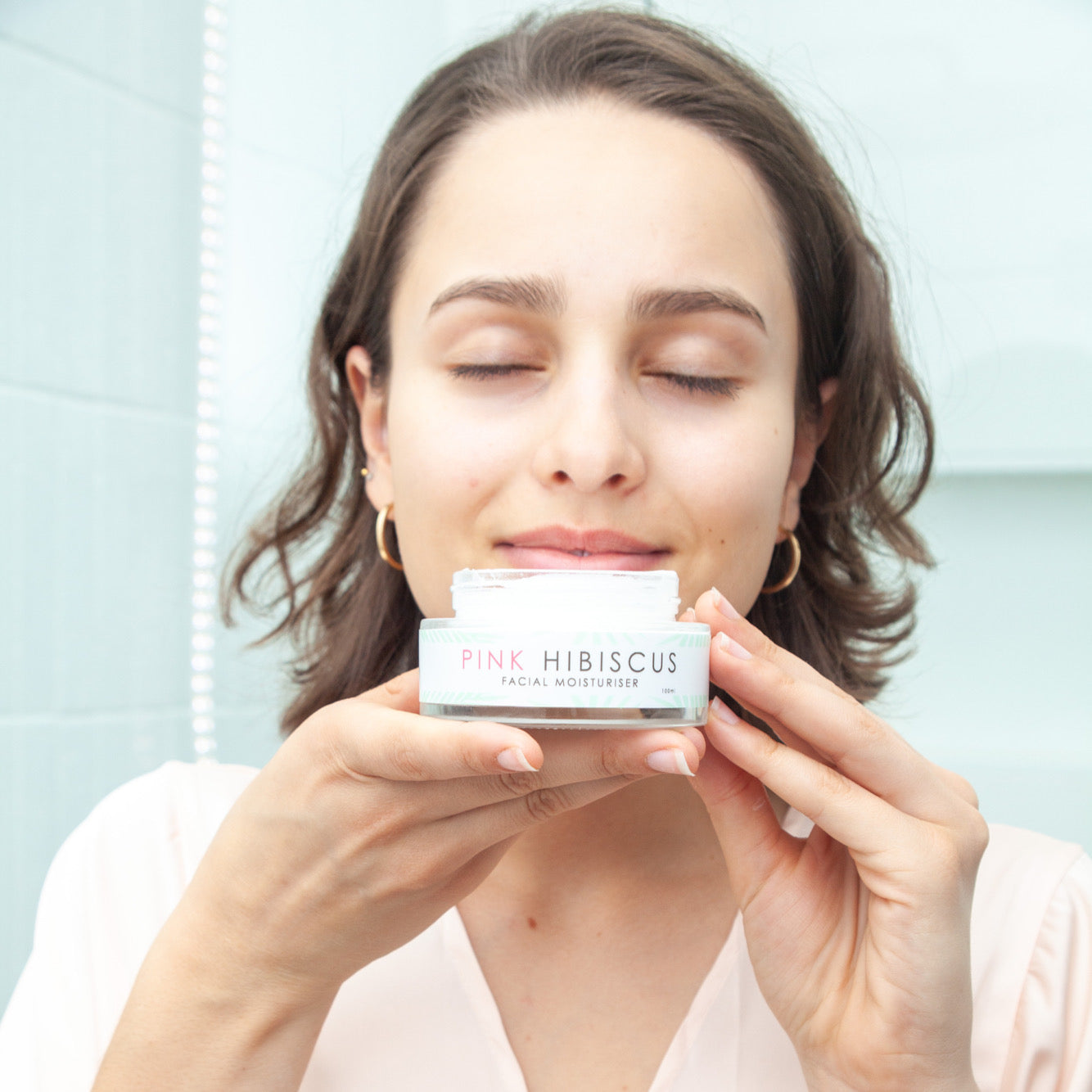 Australian woman smelling Pink Hibiscus Facial Moisturiser in pink robe