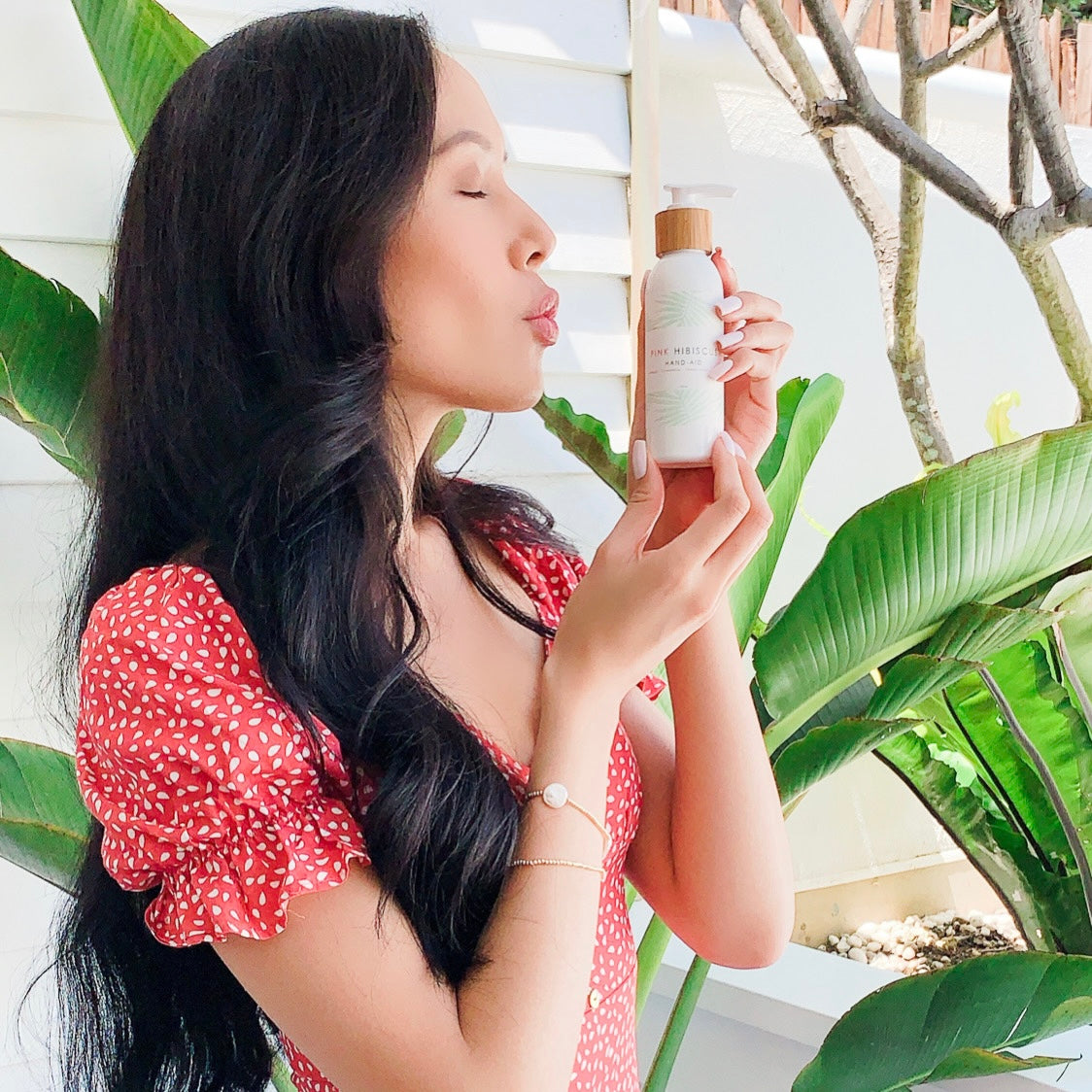 Thai woman kissing Pink Hibiscus Hand-Aid Healing Hand Balm with traveller palm behind h er