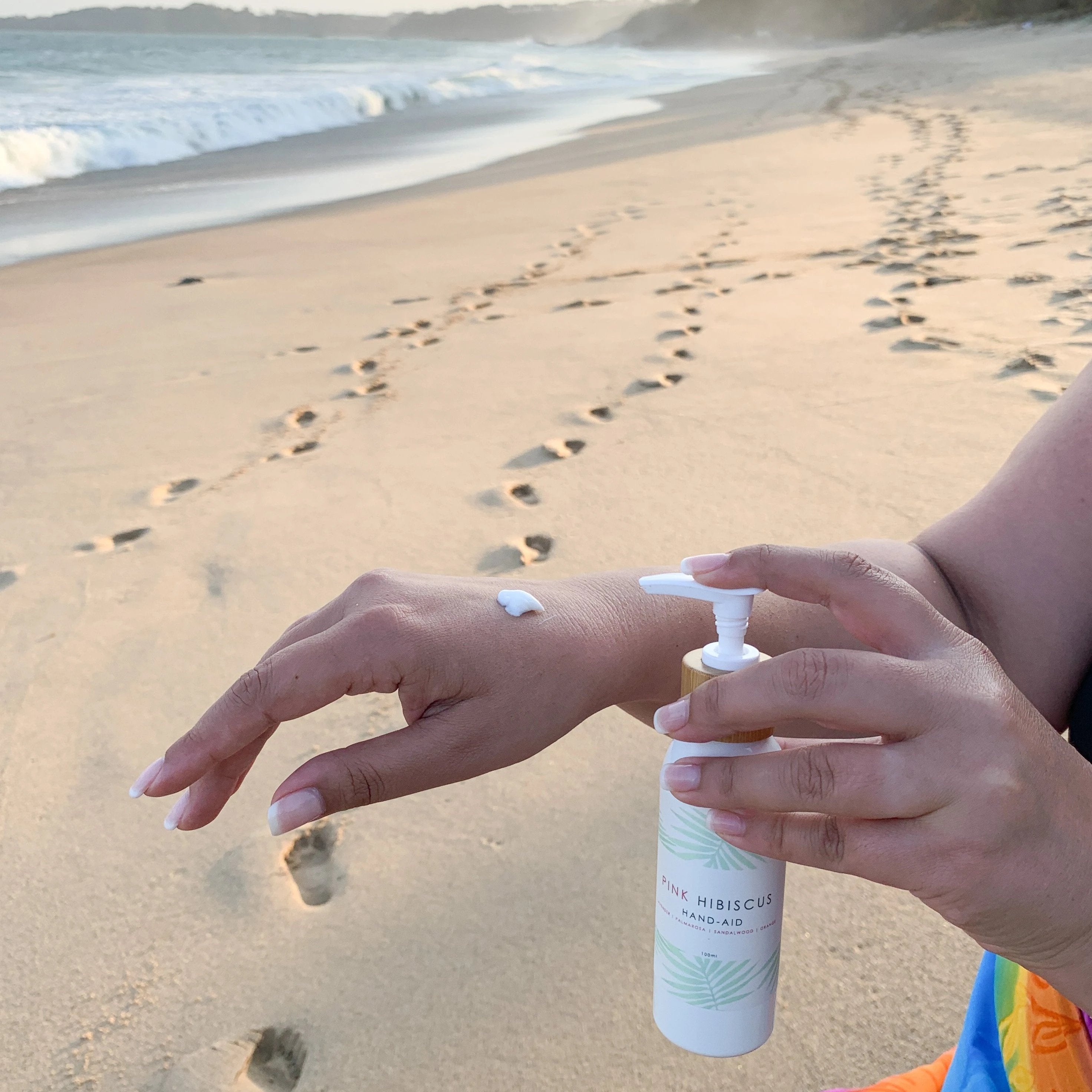 Woman applying Pink Hibiscus Hand-Aid Healing Hand Balm to hand at Coffs Harbour beach